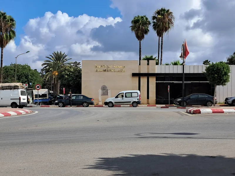 Façade de la commune d’Aïn El Aouda, avec des palmiers et la rue au premier plan.